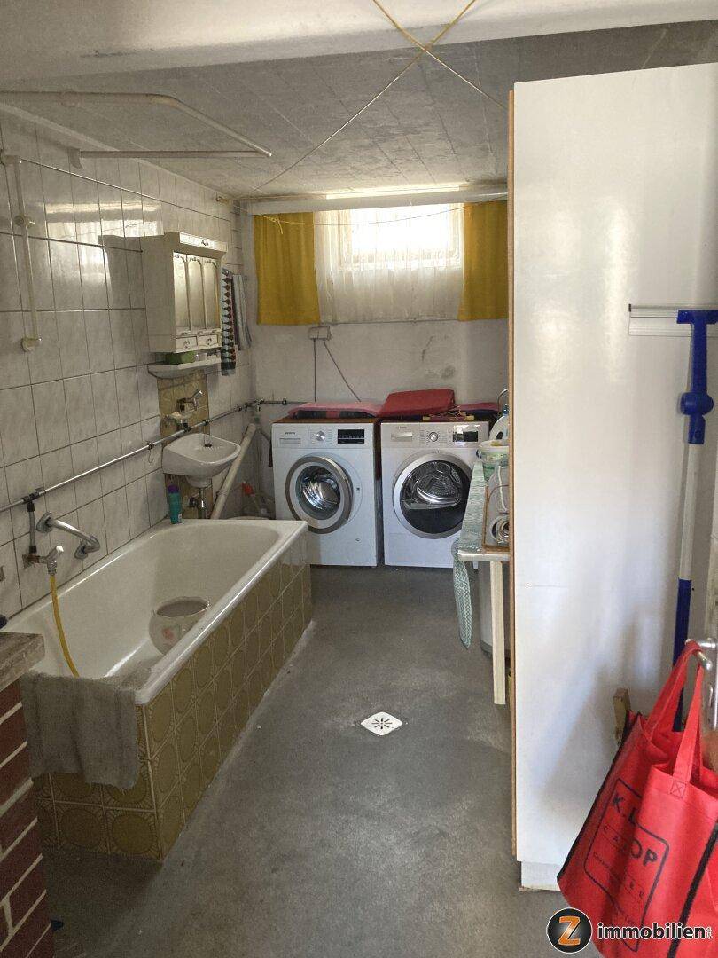 Waschküche im Keller mit Badewanne, Waschmaschinen und kleinem Fenster.