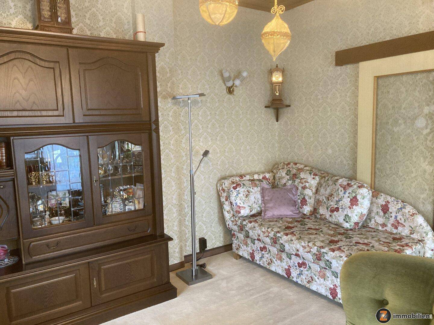 Gemütliche Sitzecke mit floral gemustertem Sofa und dunklem Holzschrank.