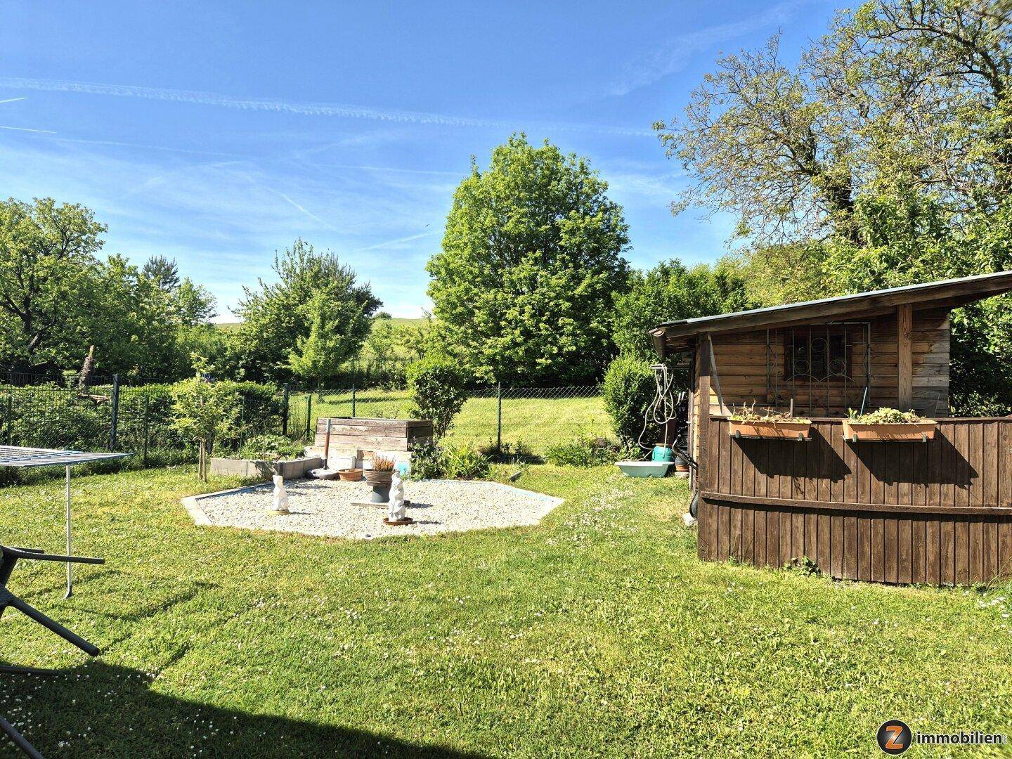 Weitläufiger Gartenbereich mit Rasen, Gartenhaus und Blick auf die grüne Umgebung.