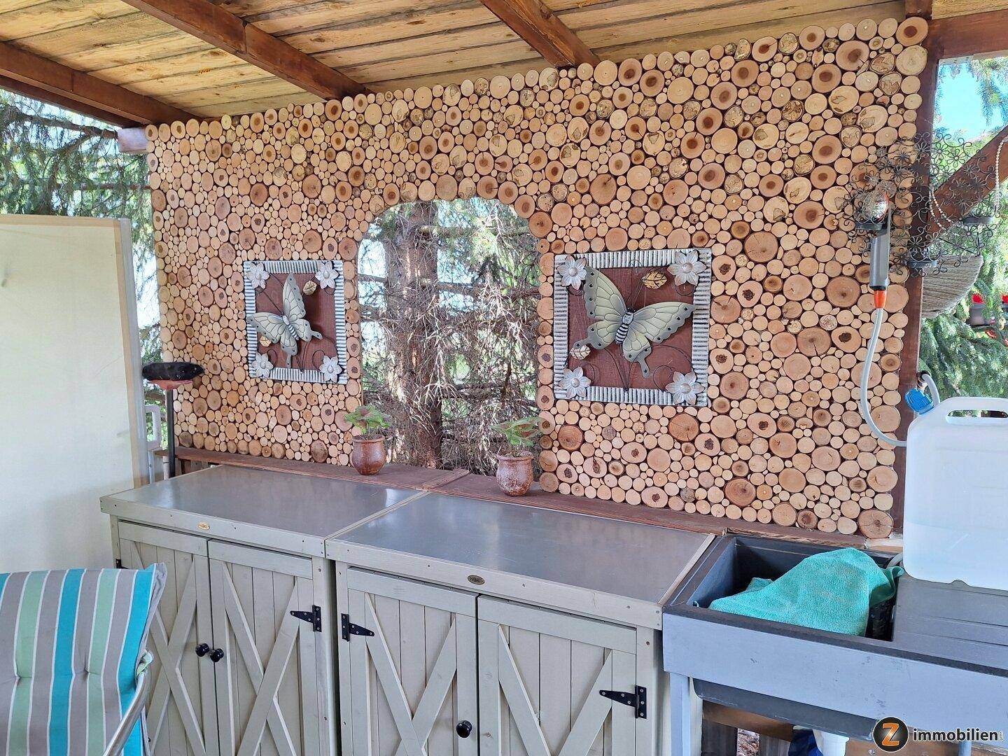 Überdachte Terrasse mit einer rustikalen Außenküche und dekorativer Holzwand.