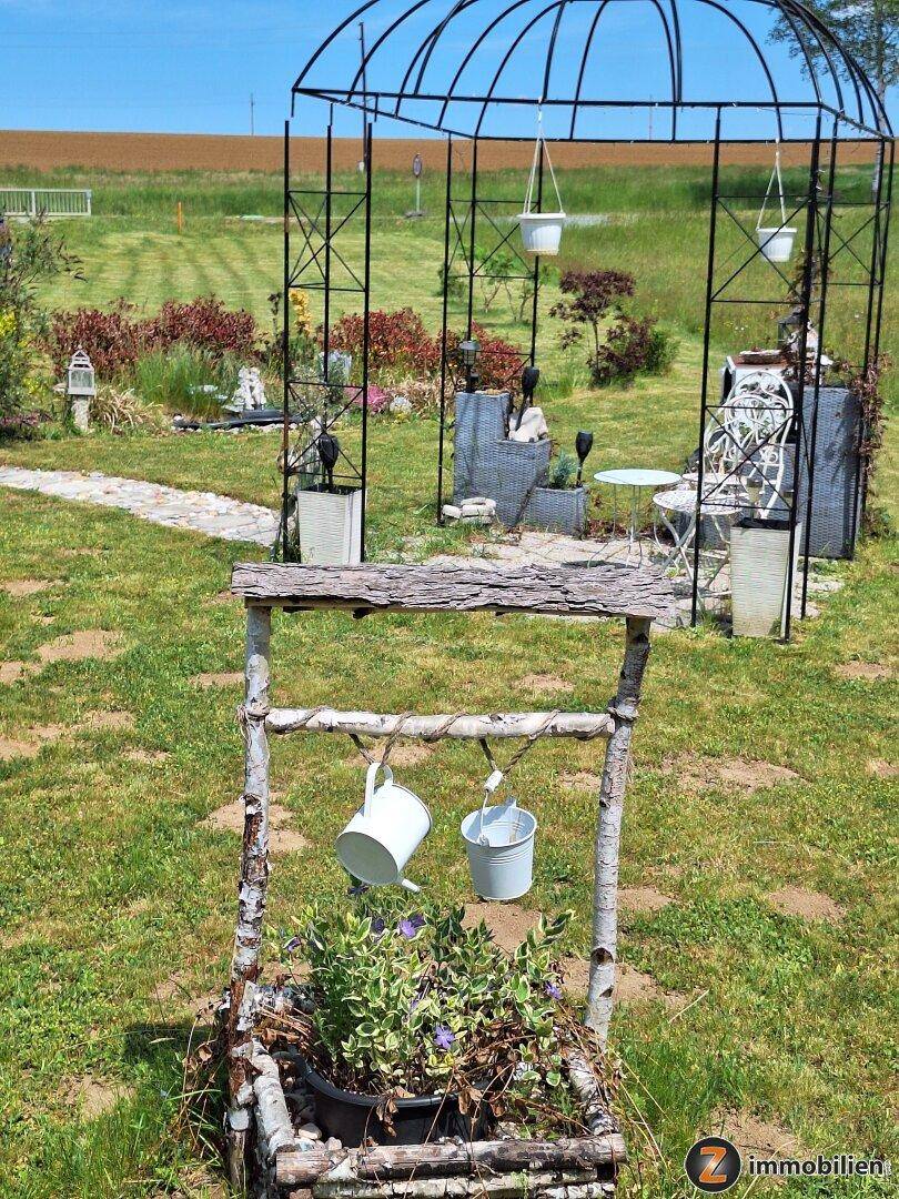 Gartenbereich mit einem Zierbrunnen und einem Metallpavillon auf einer grünen Wiese.