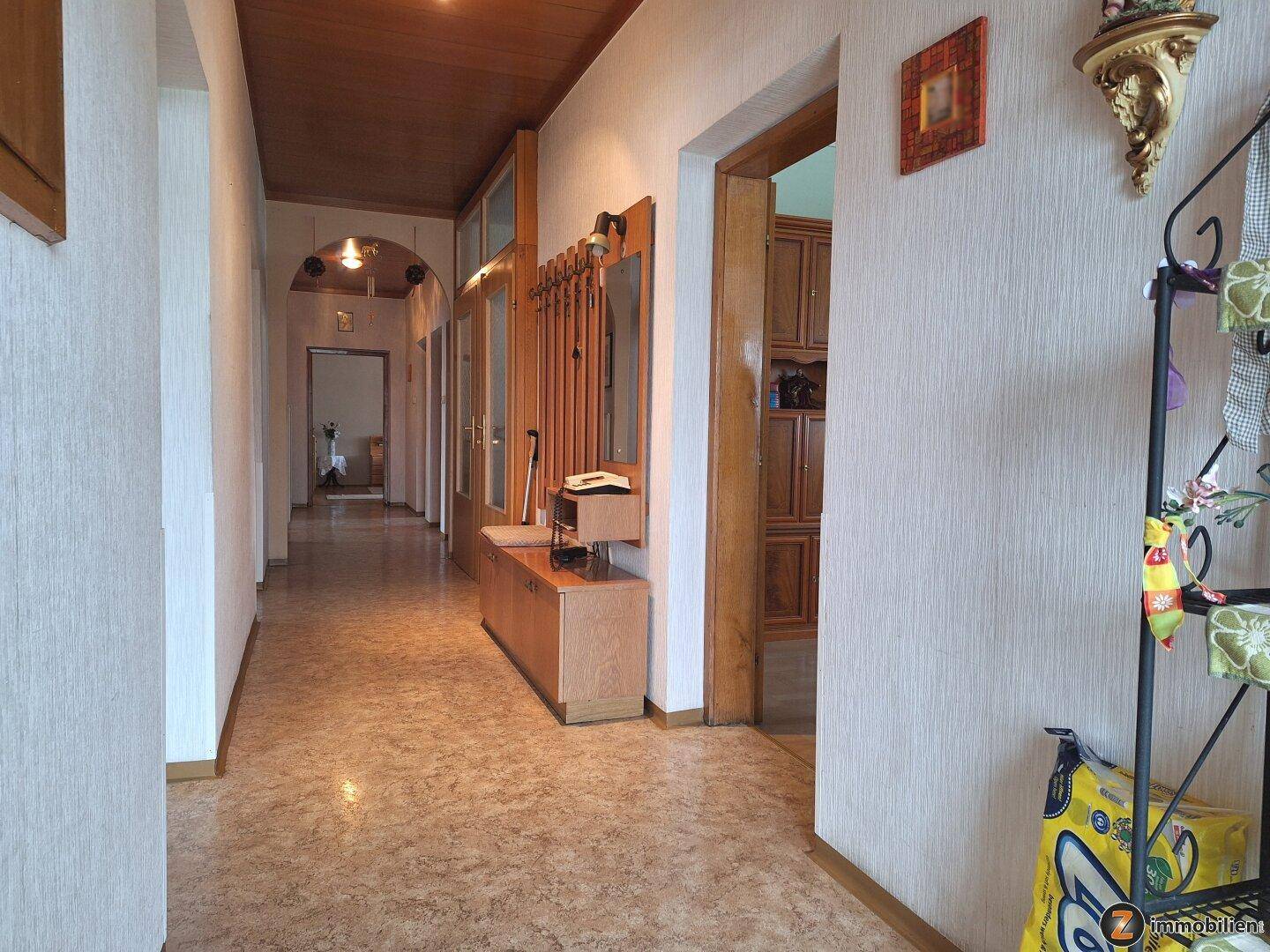 Langer Flur mit Holzdecke, gemustertem Boden und Garderobe, der zu weiteren Räumen führt.