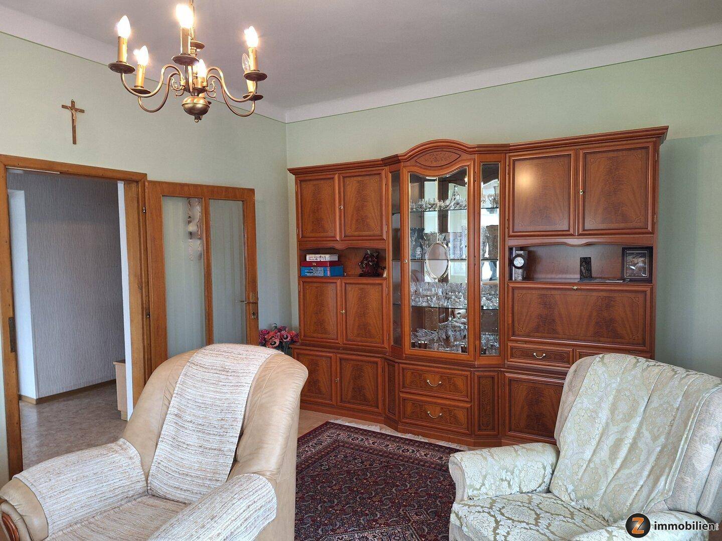 Gemütliches Wohnzimmer mit traditionellen Holzmöbeln, bequemen Sesseln und einem großen Schrank.