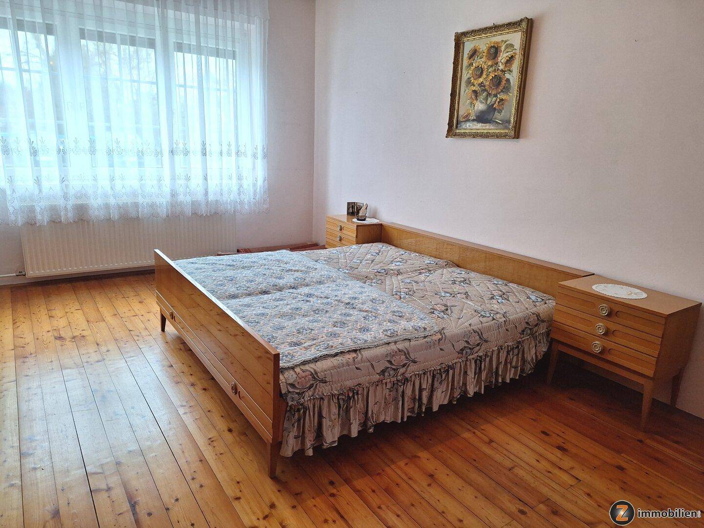 Geräumiges Schlafzimmer mit Holzboden, Doppelbett und großem Fenster für viel Tageslicht.
