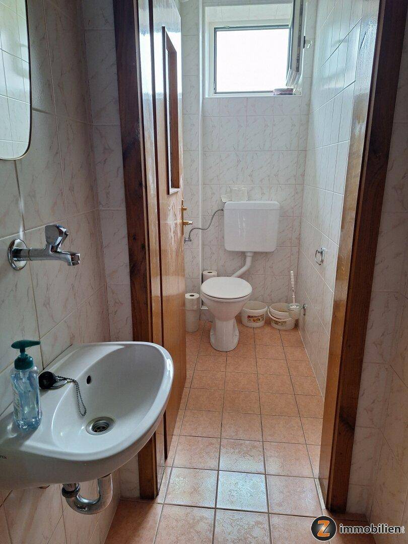 Kleines Gäste-WC mit Waschbecken, Toilette und Fenster, komplett gefliest.