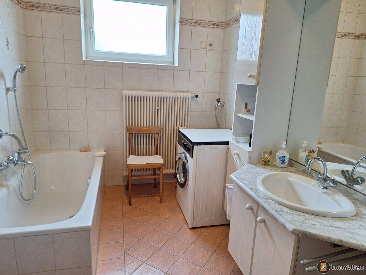 Helles Badezimmer mit Badewanne, Waschmaschine, Waschbecken und Fenster.