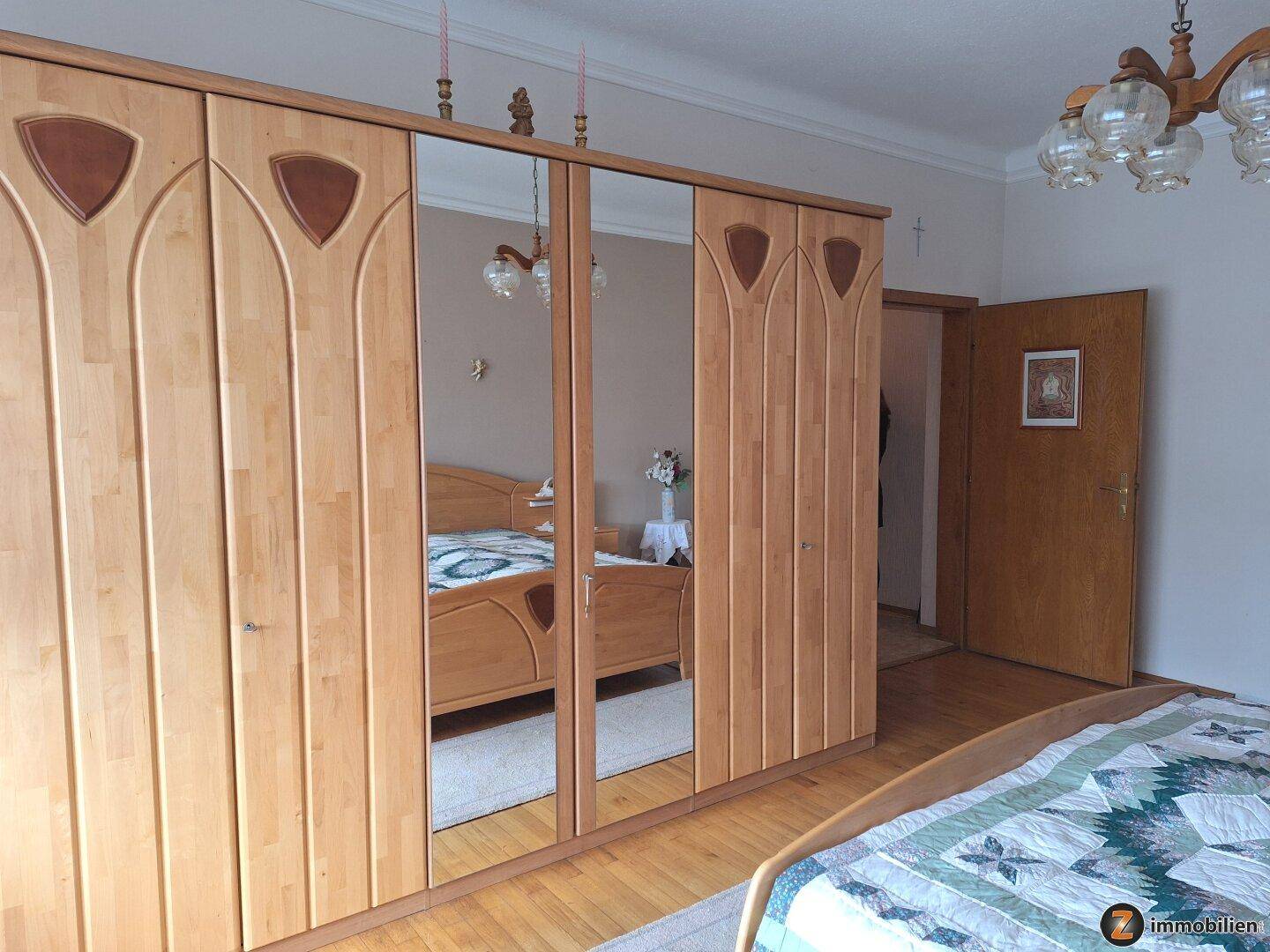 Schlafzimmer mit großem Holzschrank und Spiegeltüren, der das Bett reflektiert.