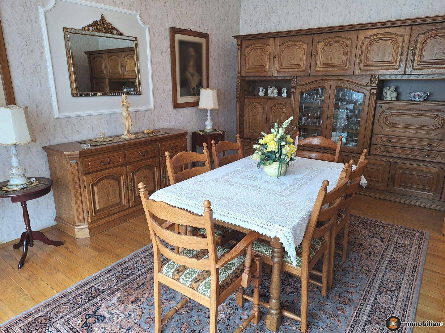 Klassischer Essbereich mit Holztisch, Stühlen und einem großen Schrank, dekoriert mit einem Spiegel.
