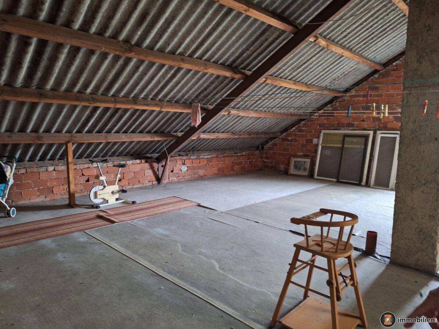 Unausgebauter Dachboden mit sichtbaren Ziegelwänden und Wellblechdach, bietet viel Stauraum.