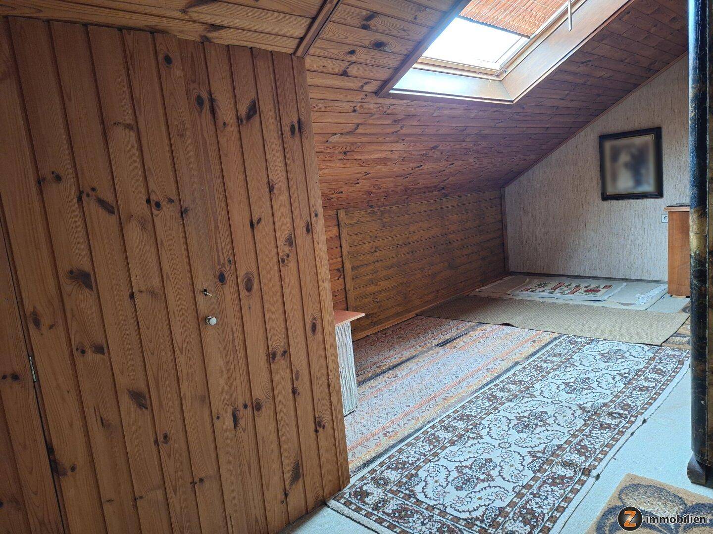 Ausgebauter Dachboden mit Holzverkleidung, Teppichboden und Dachfenster für natürliches Licht.