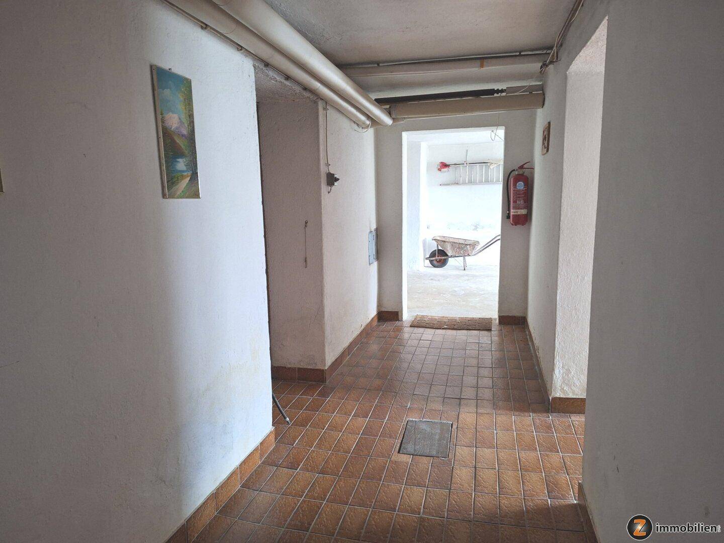 Kellerflur mit gefliestem Boden und Zugang zu weiteren Kellerräumen, ideal als Abstellfläche.