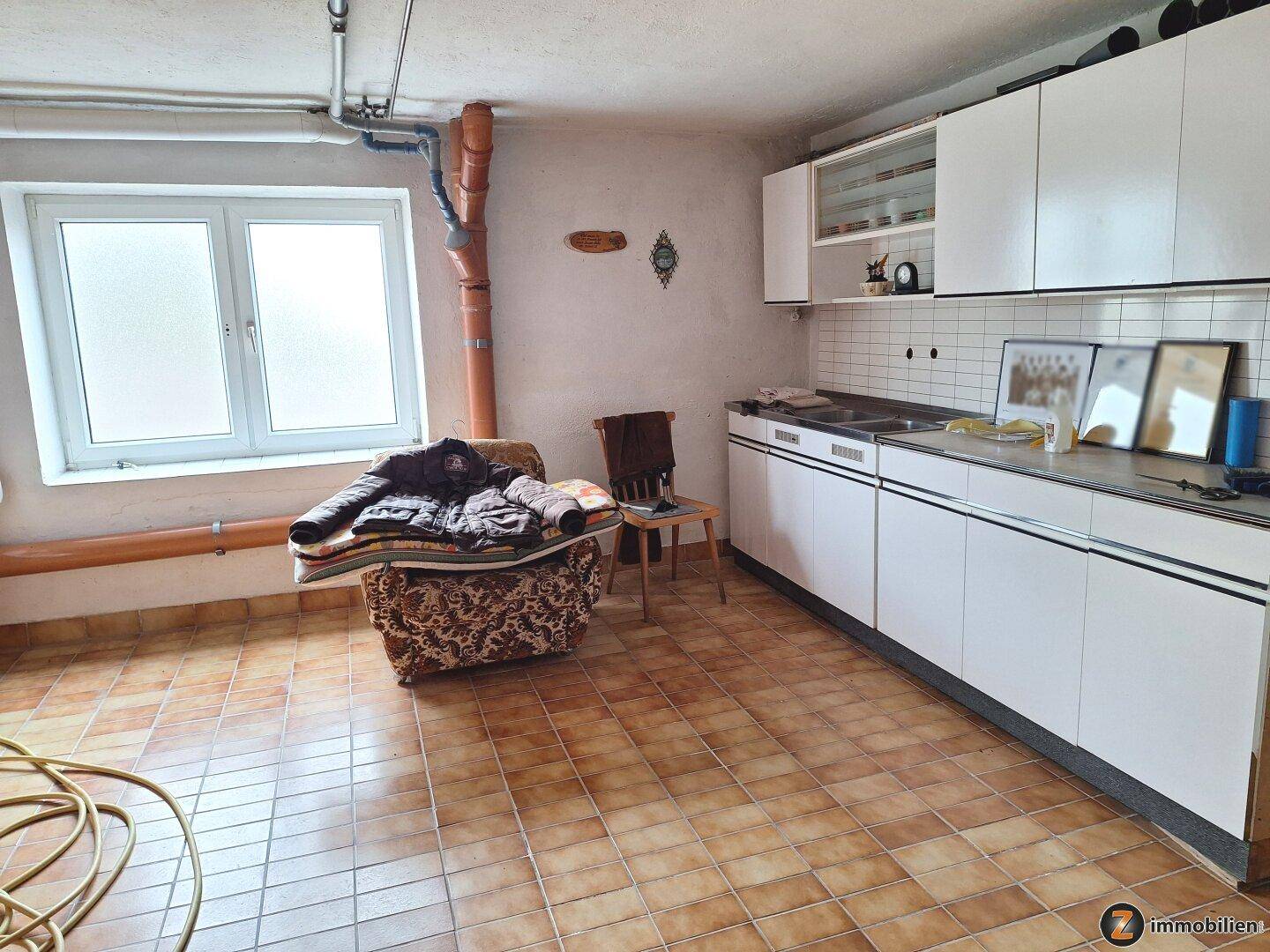 Kellerraum mit einfacher Küchenzeile, Fenster und gefliestem Boden, vielseitig nutzbar.