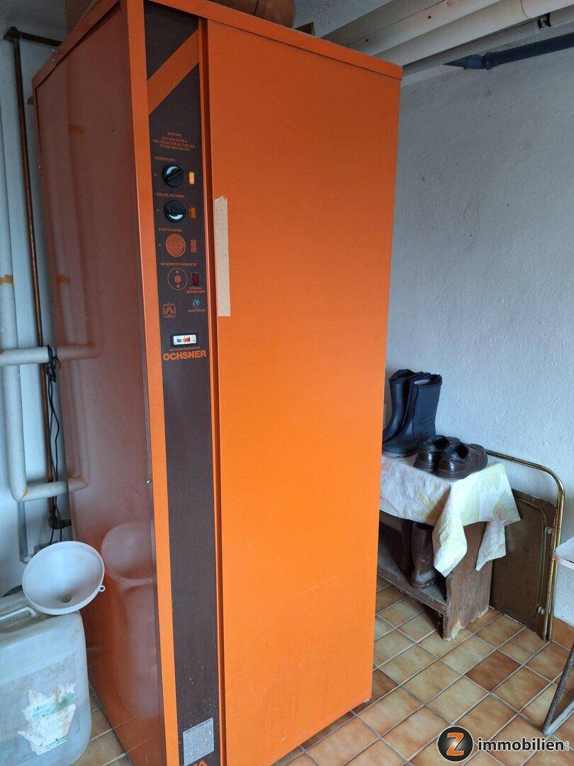 Heizungsraum mit einem großen orangefarbenen Heizkessel und gefliestem Boden.
