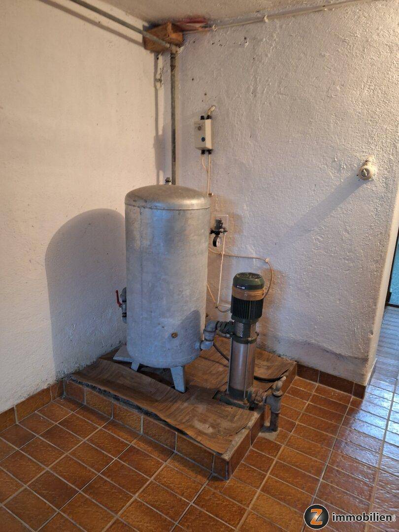 Technikraum mit Wassertank und Pumpe auf gefliestem Podest, für die Wasserversorgung.