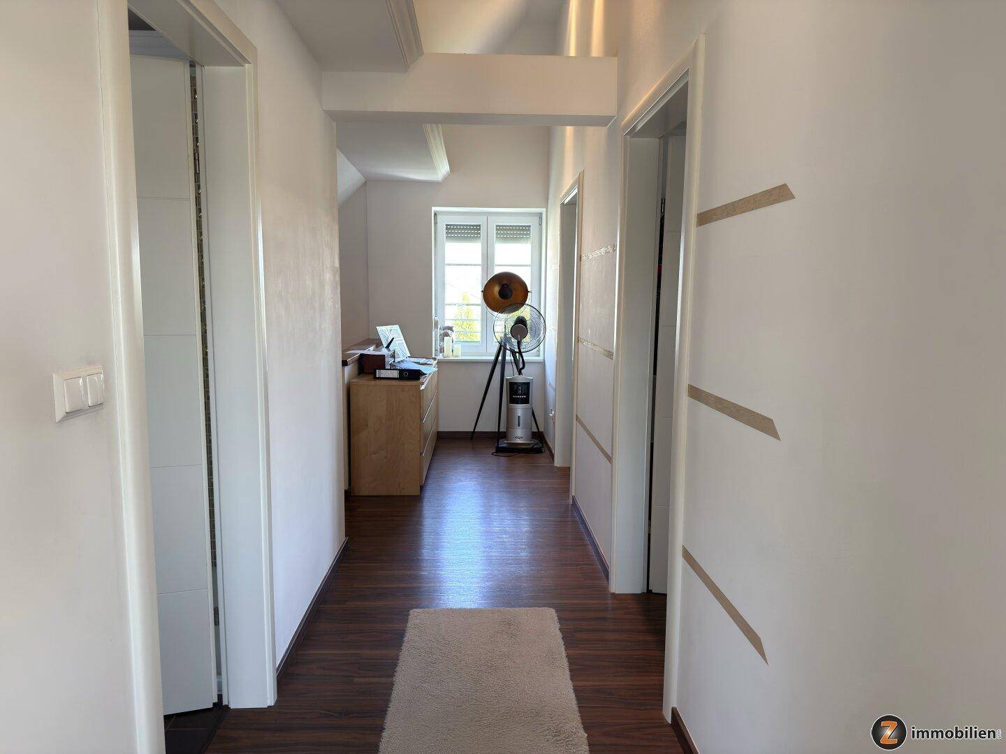 Heller Flur mit Holzboden, weißen Wänden und Blick in ein weiteres Zimmer.