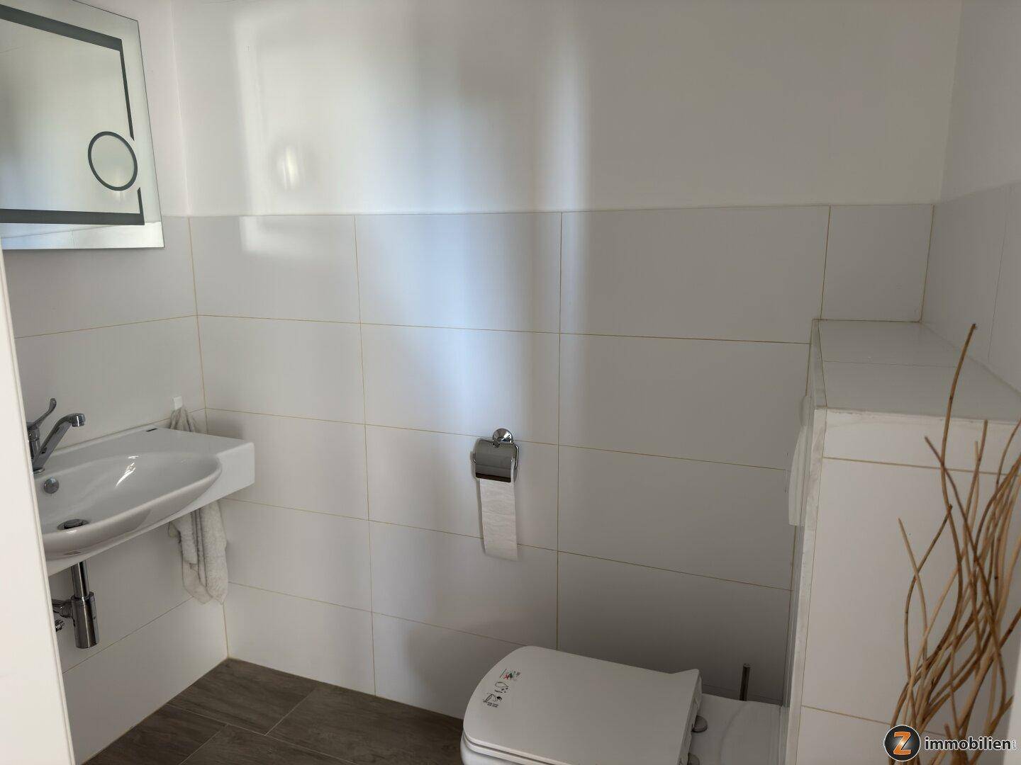 Kleines Gäste-WC mit weiß gefliesten Wänden, Waschbecken und Toilette.