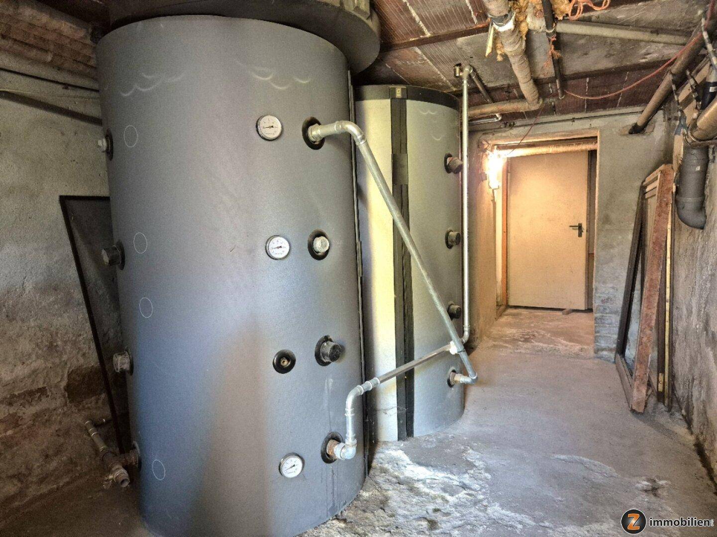 Kellerraum mit zwei großen Warmwasserspeichern und sichtbaren Rohrleitungen an der Decke.