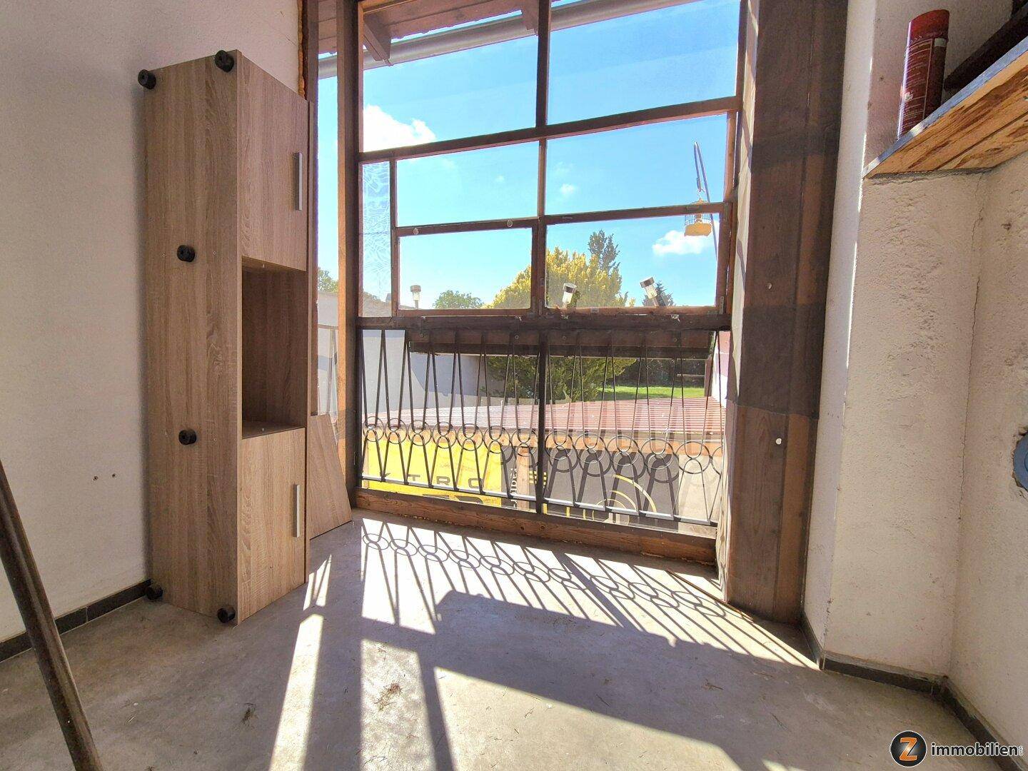 Heller Raum mit großer Fensterfront und Zugang zu einem französischen Balkon, mit Holzschränken.