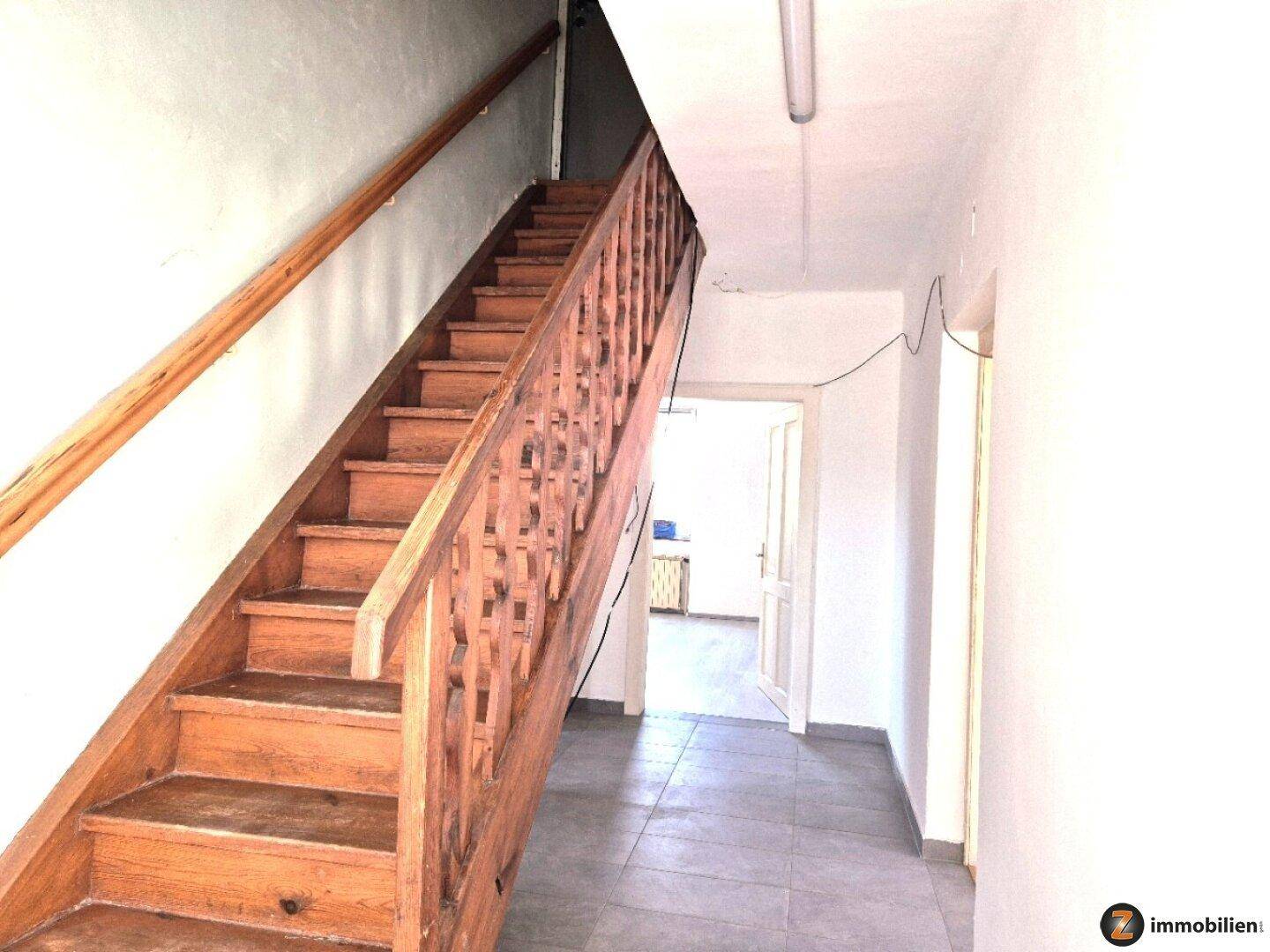 Geräumiger Flur mit einer Holztreppe und Fliesenboden, der zu den oberen Etagen führt.