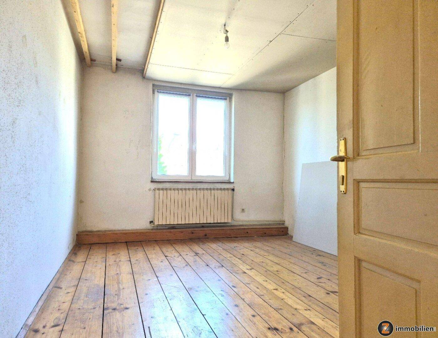 Helles Zimmer mit Dielenboden, weißen Wänden und einem Fenster, ideal als Schlafzimmer.
