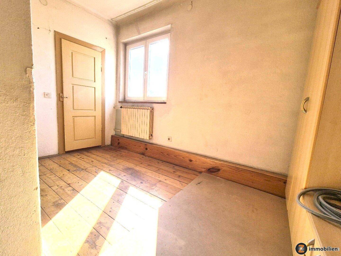 Gemütliches Zimmer mit Dielenboden, weißen Wänden und einem Fenster, bereit zur Renovierung.