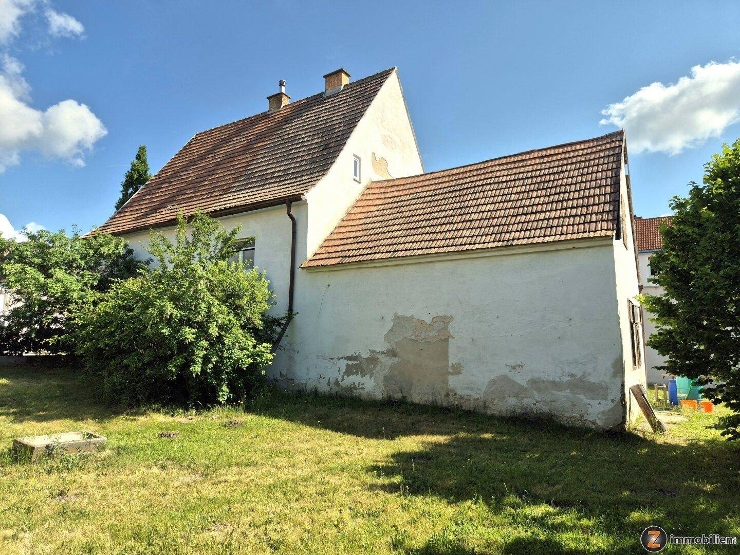 Rückansicht des Hauses mit Ziegeldach und sichtbaren Putzschäden an der Fassade.