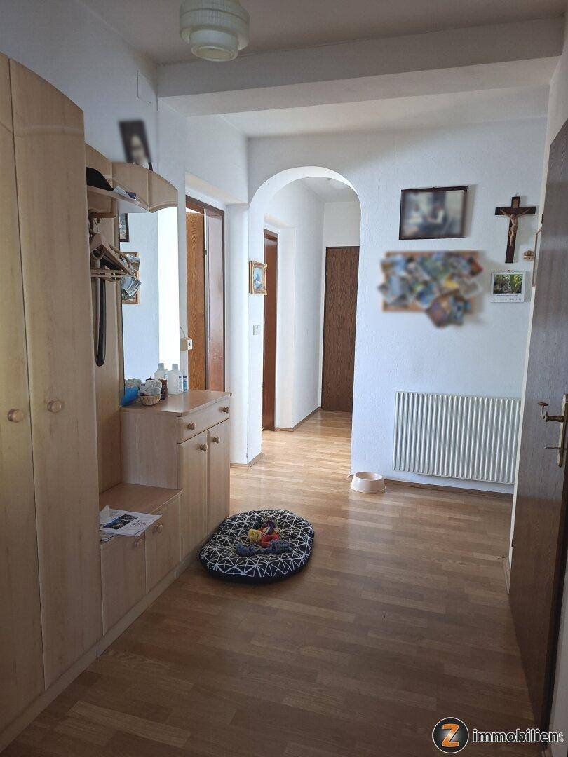 Heller Flur mit Holzfußboden, Garderobe und einem Bogen zum weiteren Wohnbereich.