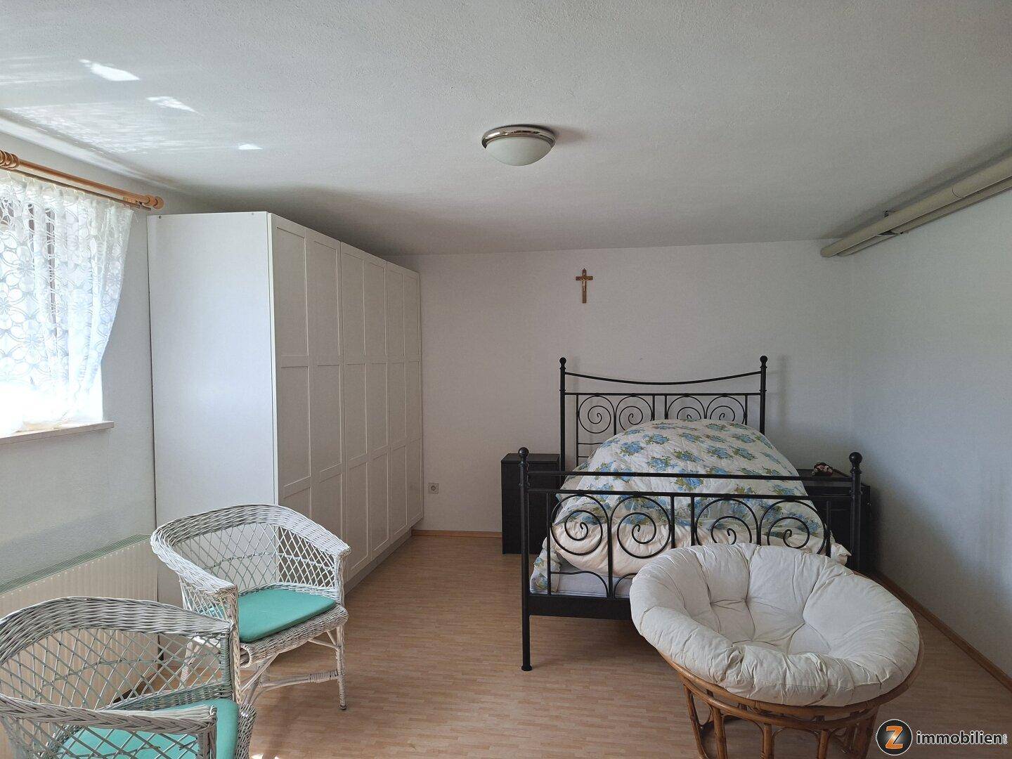 Schlafzimmer mit Doppelbett, großem Kleiderschrank und Korbsesseln am Fenster.