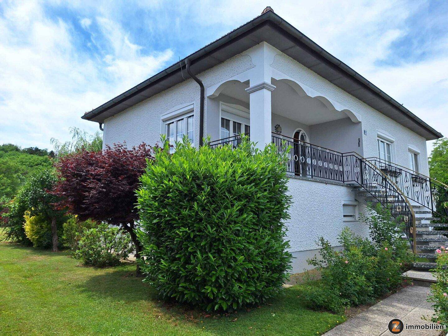 Seitenansicht des Hauses mit überdachtem Eingangsbereich, Treppe und gepflegter Gartenanlage.
