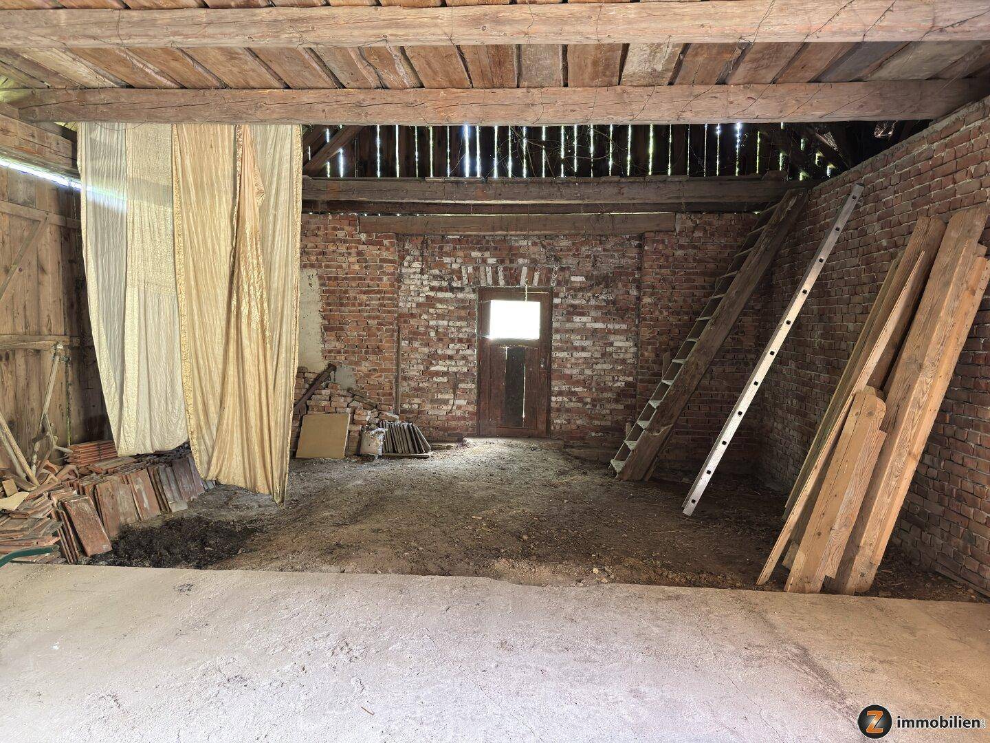 Geräumiger Scheunenraum mit Holzbalken, Ziegelwänden und einem Fenster.
