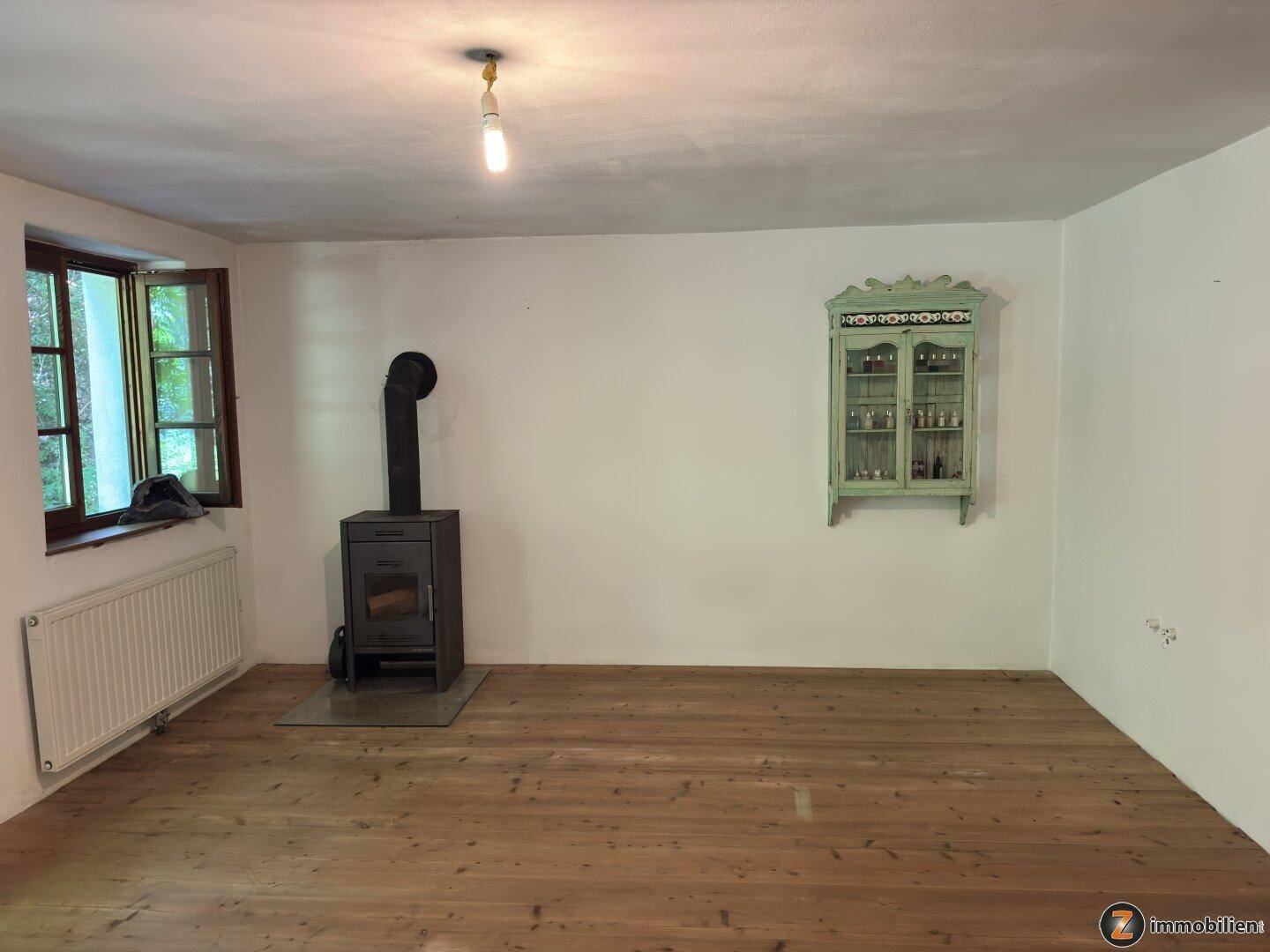 Helles Wohnzimmer mit Holzboden, einem Kaminofen und einem dekorativen Wandschrank.