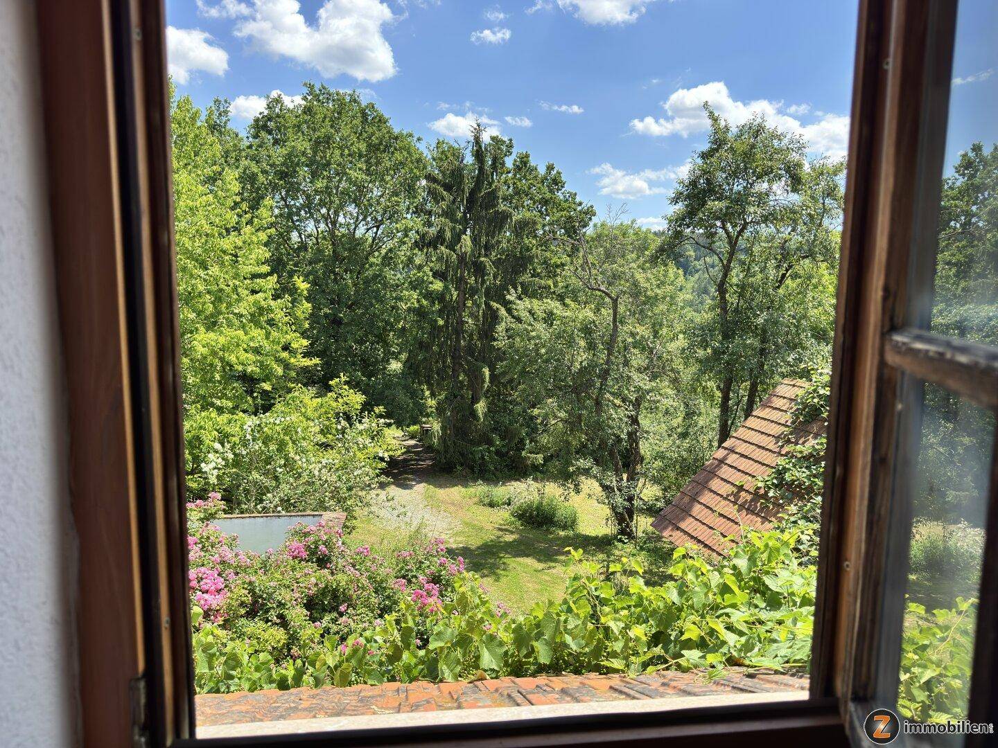 Malerischer Ausblick aus einem Fenster auf einen üppigen Garten und die umliegende Natur.