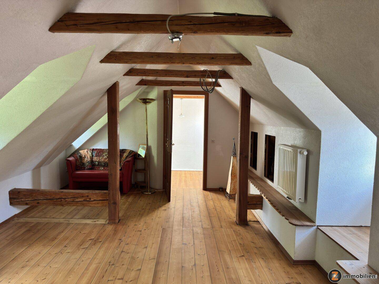 Gemütlicher Dachbodenraum mit sichtbaren Holzbalken, Holzboden und einer Sitzecke.