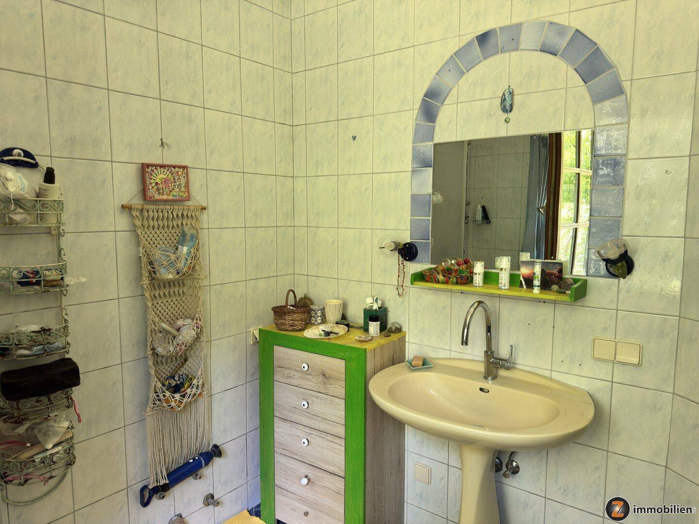 Badezimmer mit Waschbecken, Spiegel und hellblauen Fliesen an den Wänden.