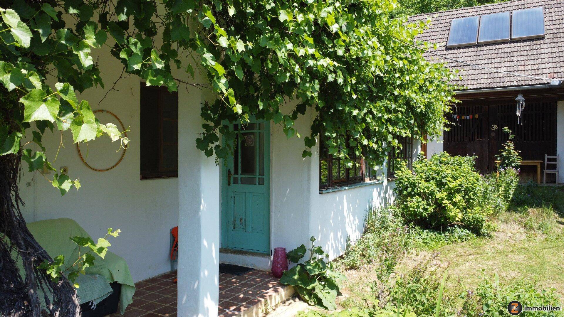 Überdachte Terrasse mit Sitzgelegenheit und Blick auf das grüne Grundstück und das Haus.