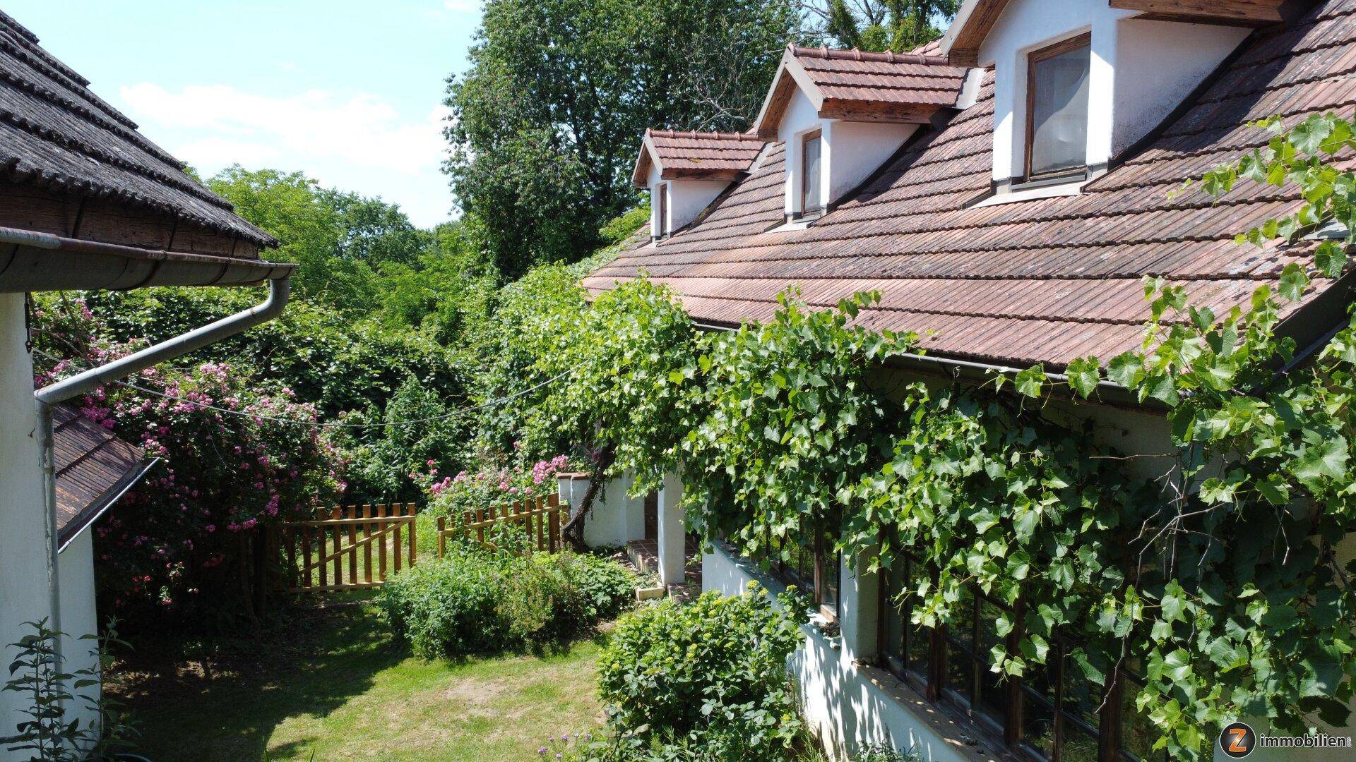 Seitenansicht des Hauses mit Dachgauben, bewachsener Fassade und üppiger Vegetation im Gartenbereich.