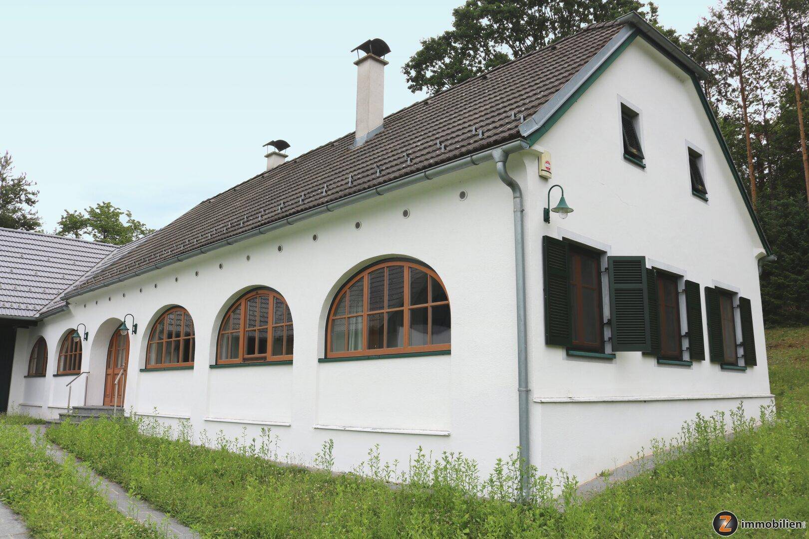 Seitenansicht des Landhauses mit Rundbogenfenstern und grünen Fensterläden.
