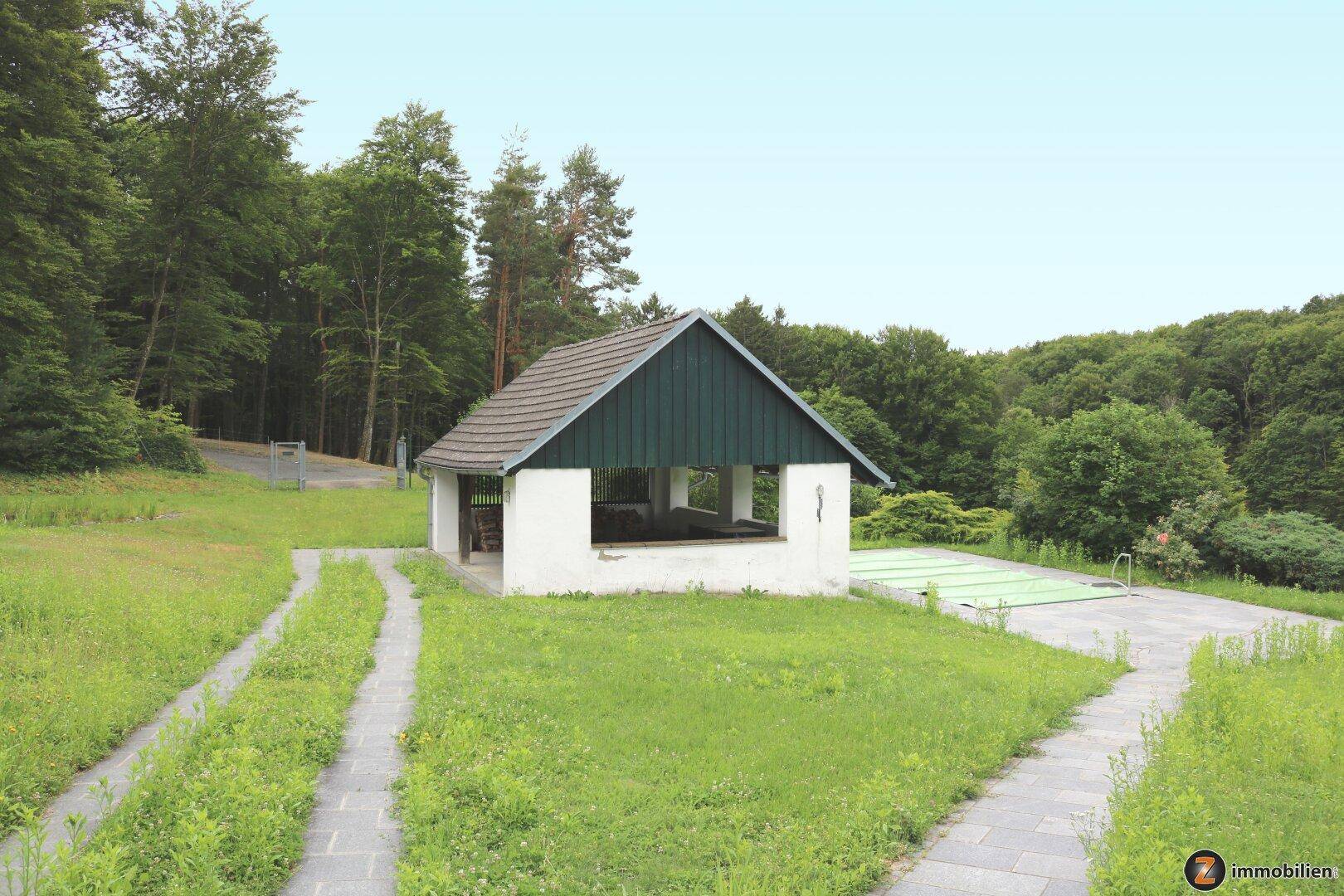Außenbereich mit Nebengebäude, Pool und weitläufiger Grünfläche.