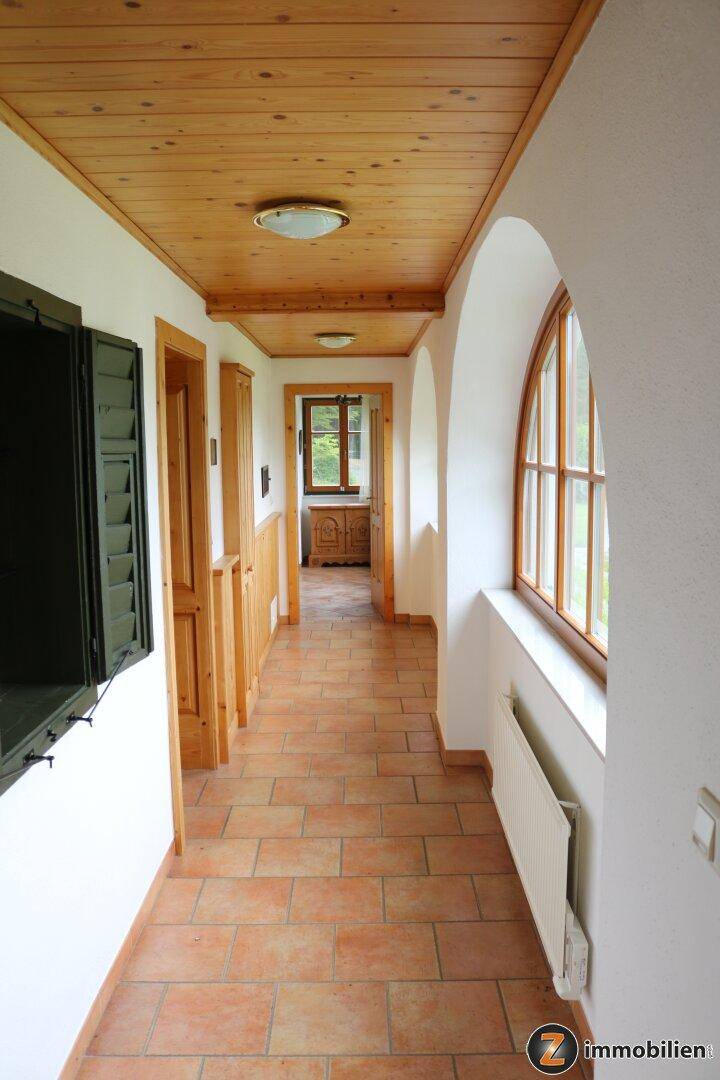 Heller Flur mit Terrakottafliesen, Holzdecke und Rundbogenfenster.