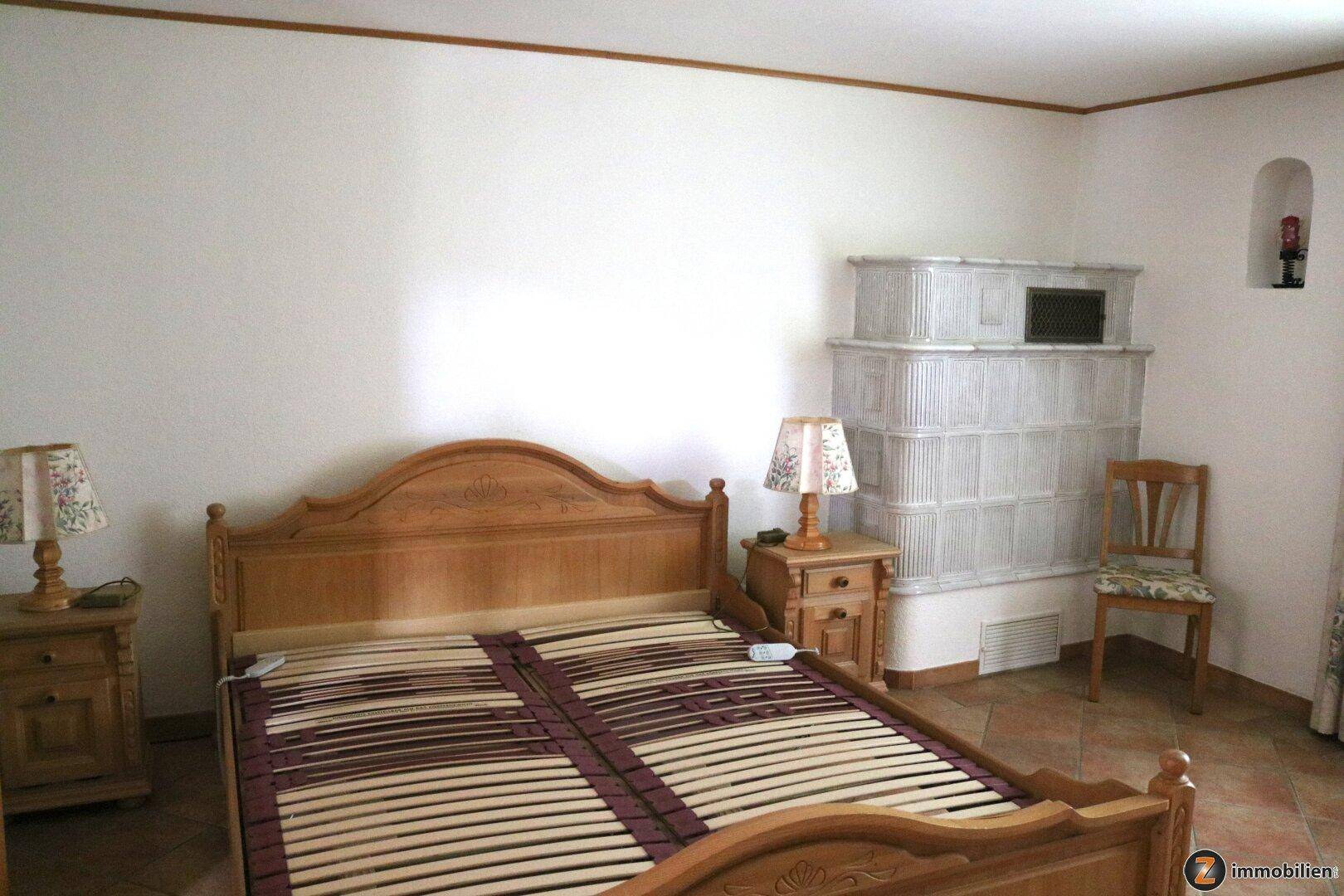 Schlafzimmer mit Holzbett, Nachttischen und einem weißen Kachelofen.