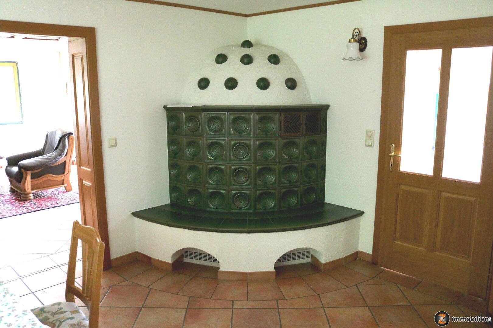 Heller Raum mit einem weiteren traditionellen Kachelofen und Terrakottafliesen.