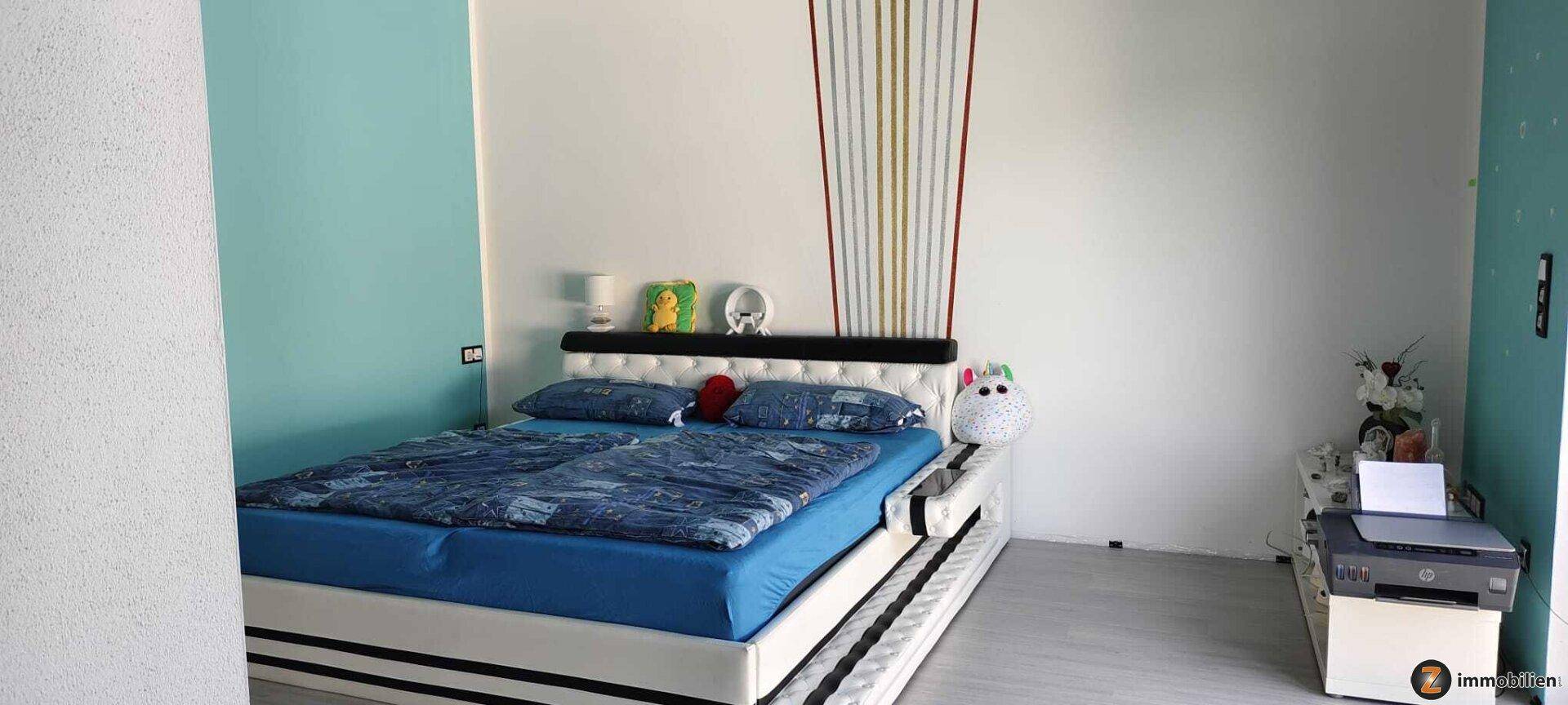 Schlafzimmer mit modernem Bett, farbiger Wandgestaltung und viel Tageslicht.