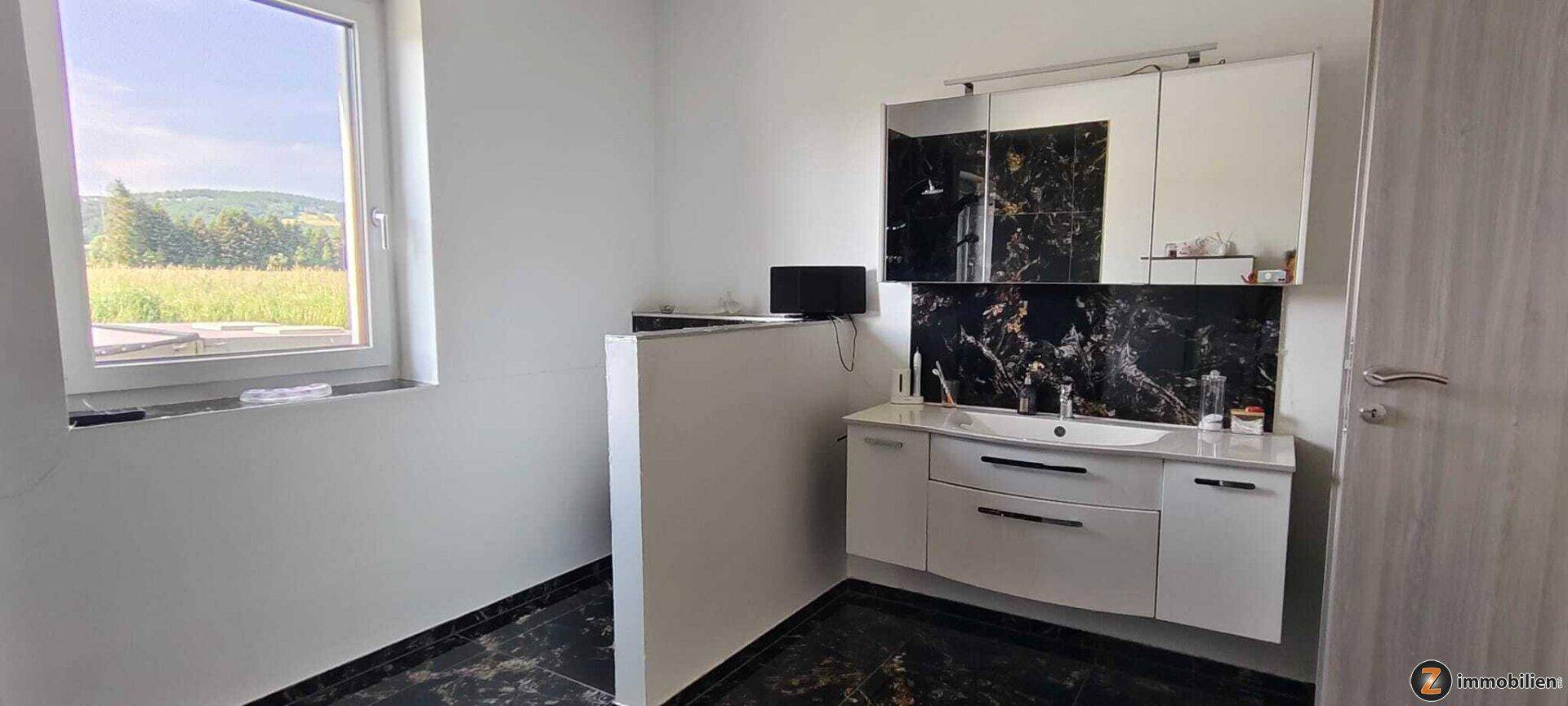 Helles Badezimmer mit Waschtisch, Spiegelschrank und Fenster mit Weitblick.