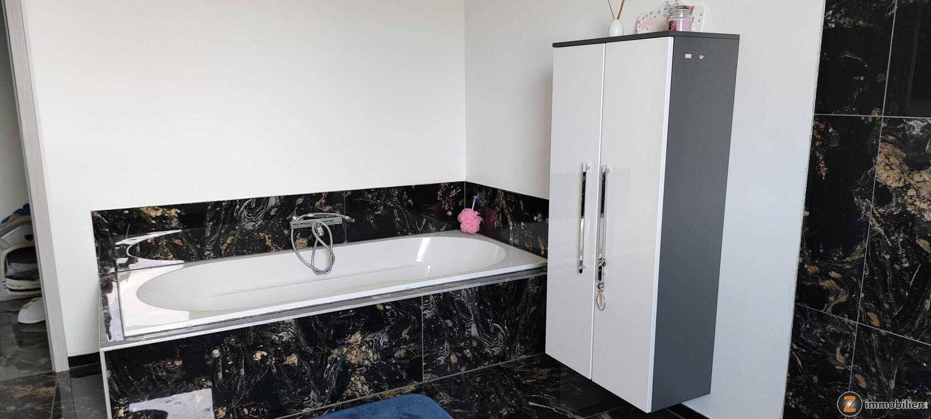 Badezimmer mit Badewanne, dunklen Marmorfliesen und praktischem Hochschrank.