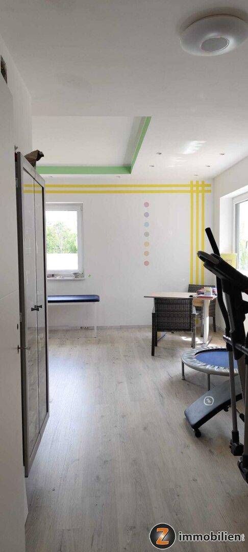 Fitnessraum mit Sportgeräten, Fenster und farbiger Decken- und Wandgestaltung.