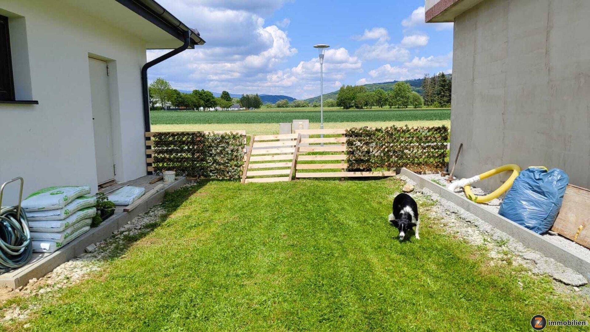 Gepflegter Gartenbereich mit Rasenfläche, Hecke und Blick auf die Landschaft.