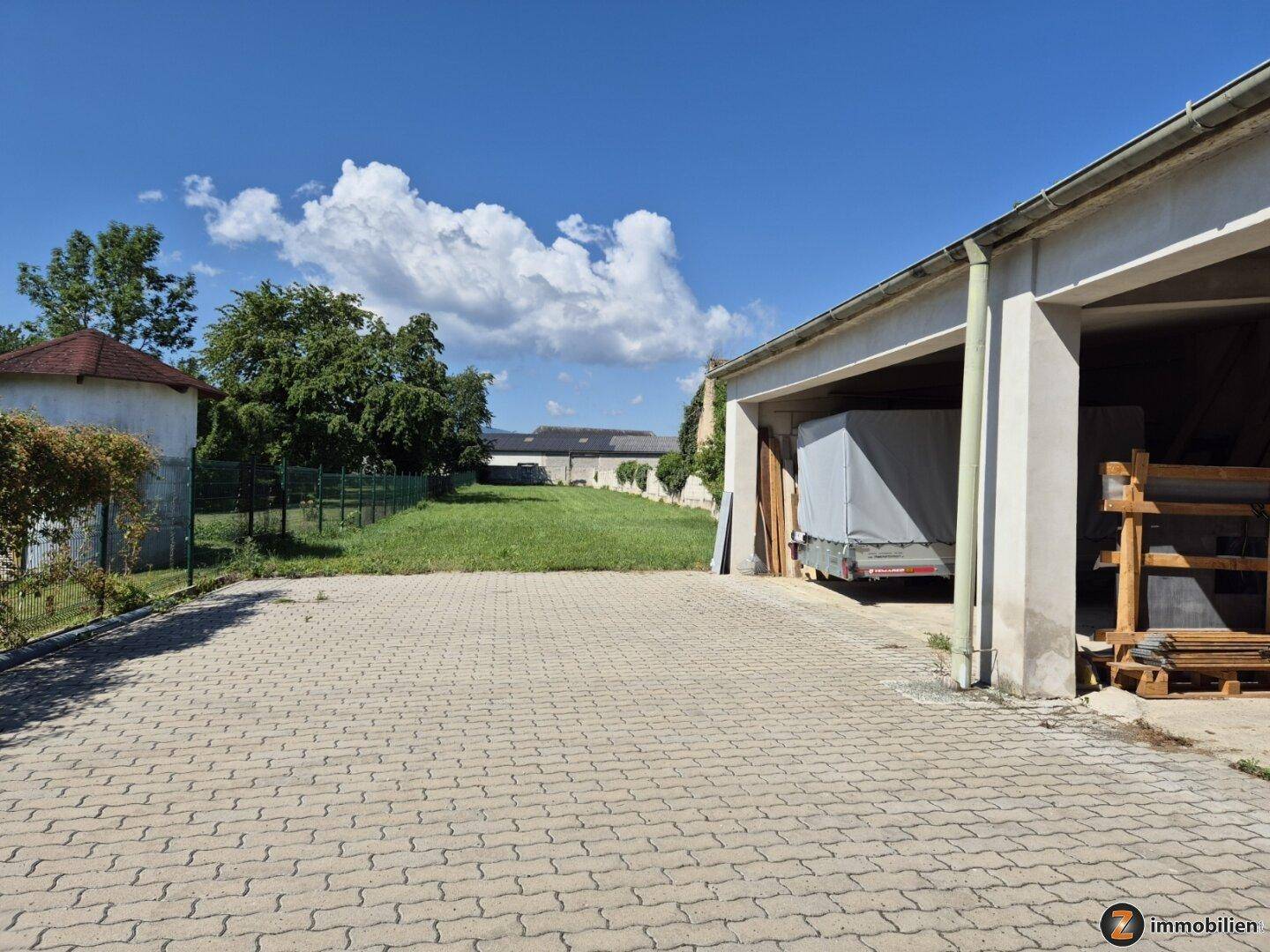 Gepflasterte Einfahrt führt zu einer Garage und einem weiteren Gebäude im Hintergrund.