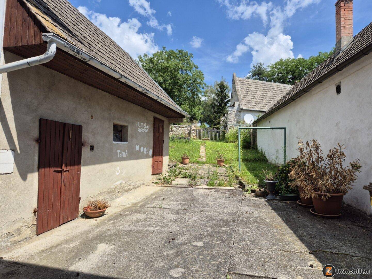 Gepflasterter Hofbereich zwischen zwei Gebäuden mit Zugang zum Garten.