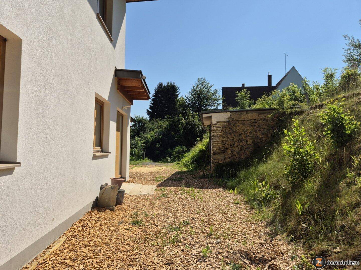 Seitenansicht des Hauses mit weißer Fassade und einem mit Holzhackschnitzeln bedeckten Weg.