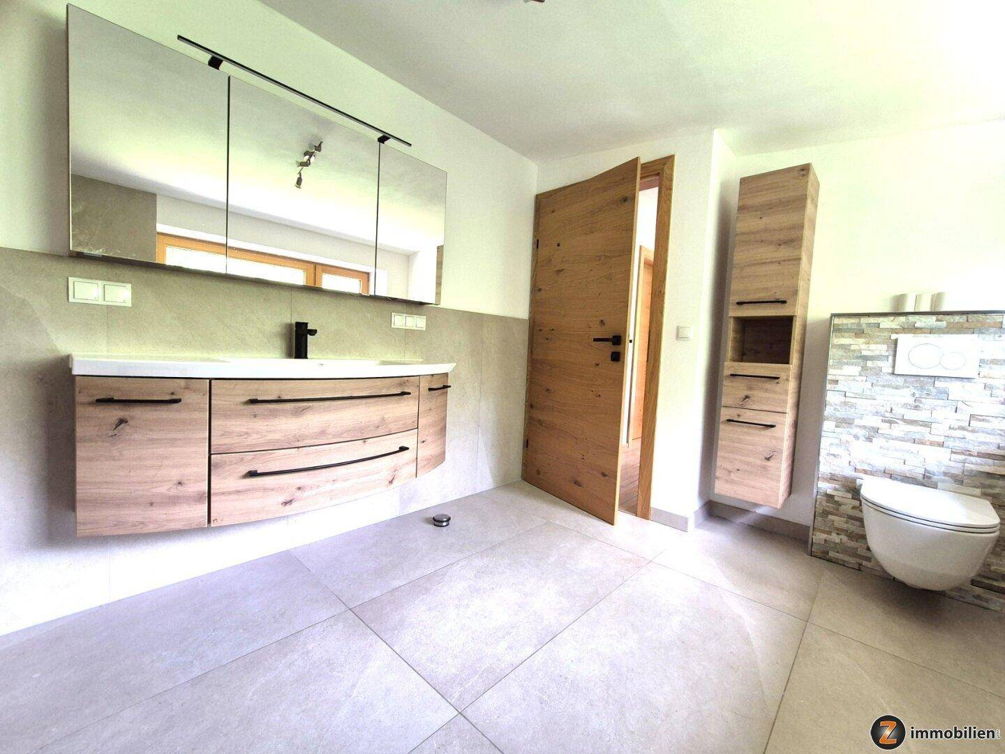 Modernes Badezimmer mit großem Waschtisch, Spiegelschrank und Wand-WC, hell gefliest.